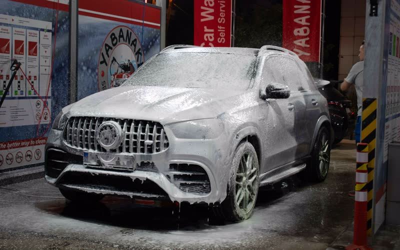 Ασημί SUV σκεπασμένο με πυκνό λευκό αφρό μέσα στη θέση πλύσης του Yabanaki